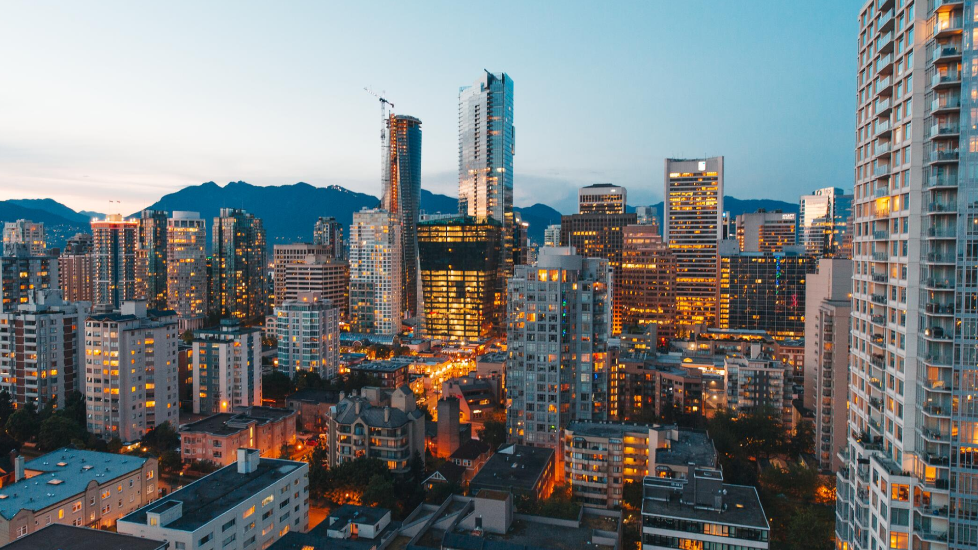 City skyline at dusk with illuminated high-rise buildings and mountains in the background.