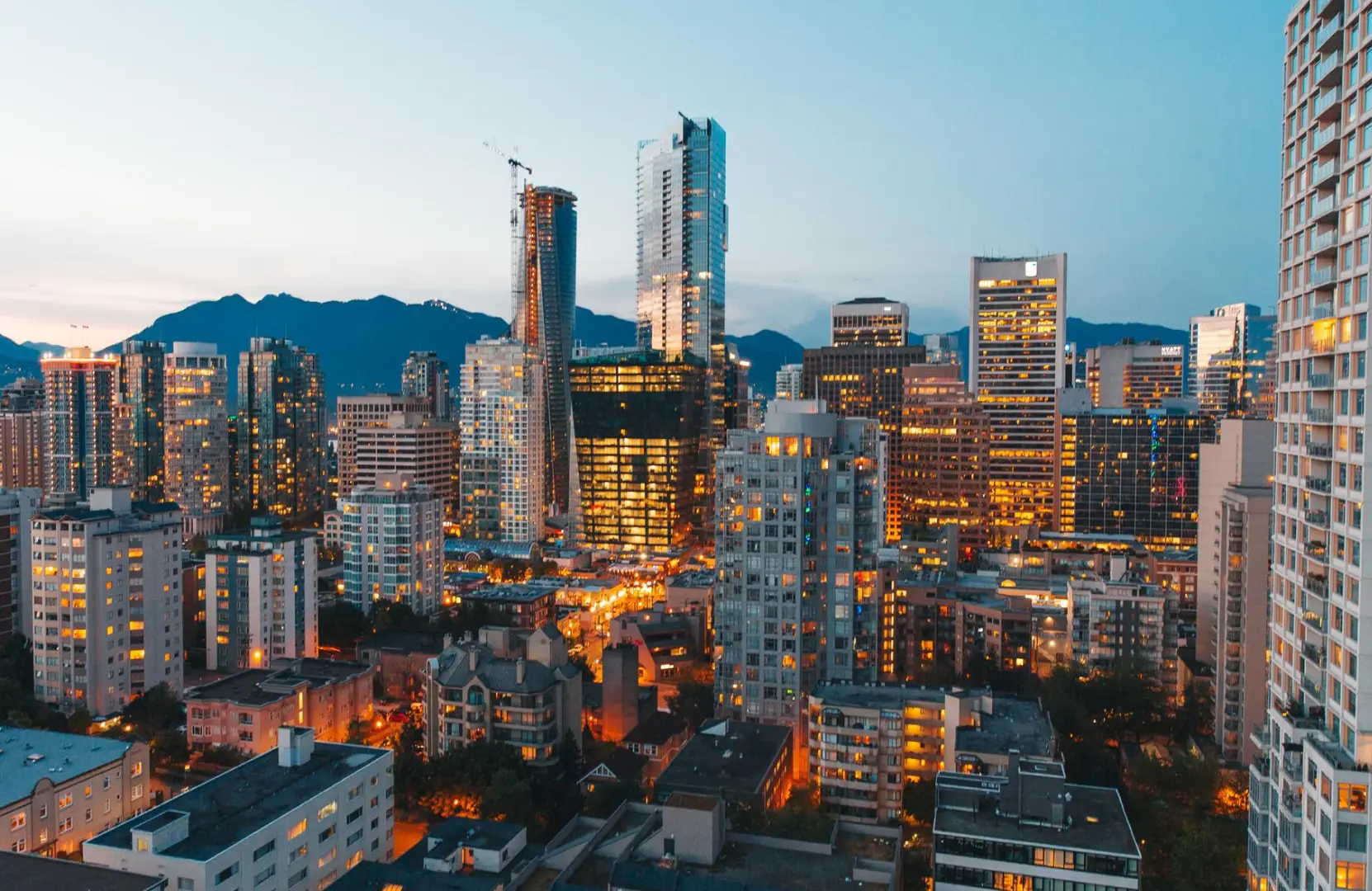City skyline at dusk with illuminated high-rise buildings and mountains in the background.