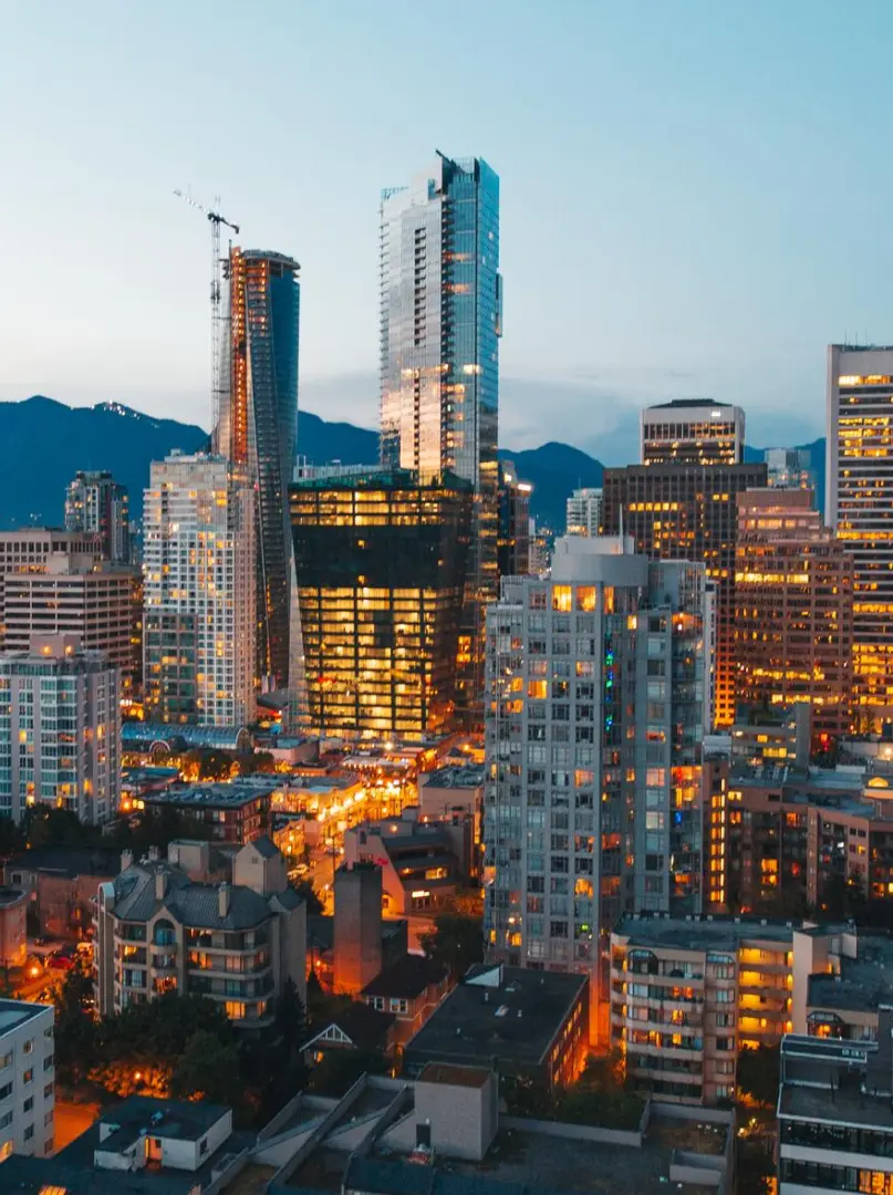 City skyline at dusk with illuminated high-rise buildings and mountains in the background.