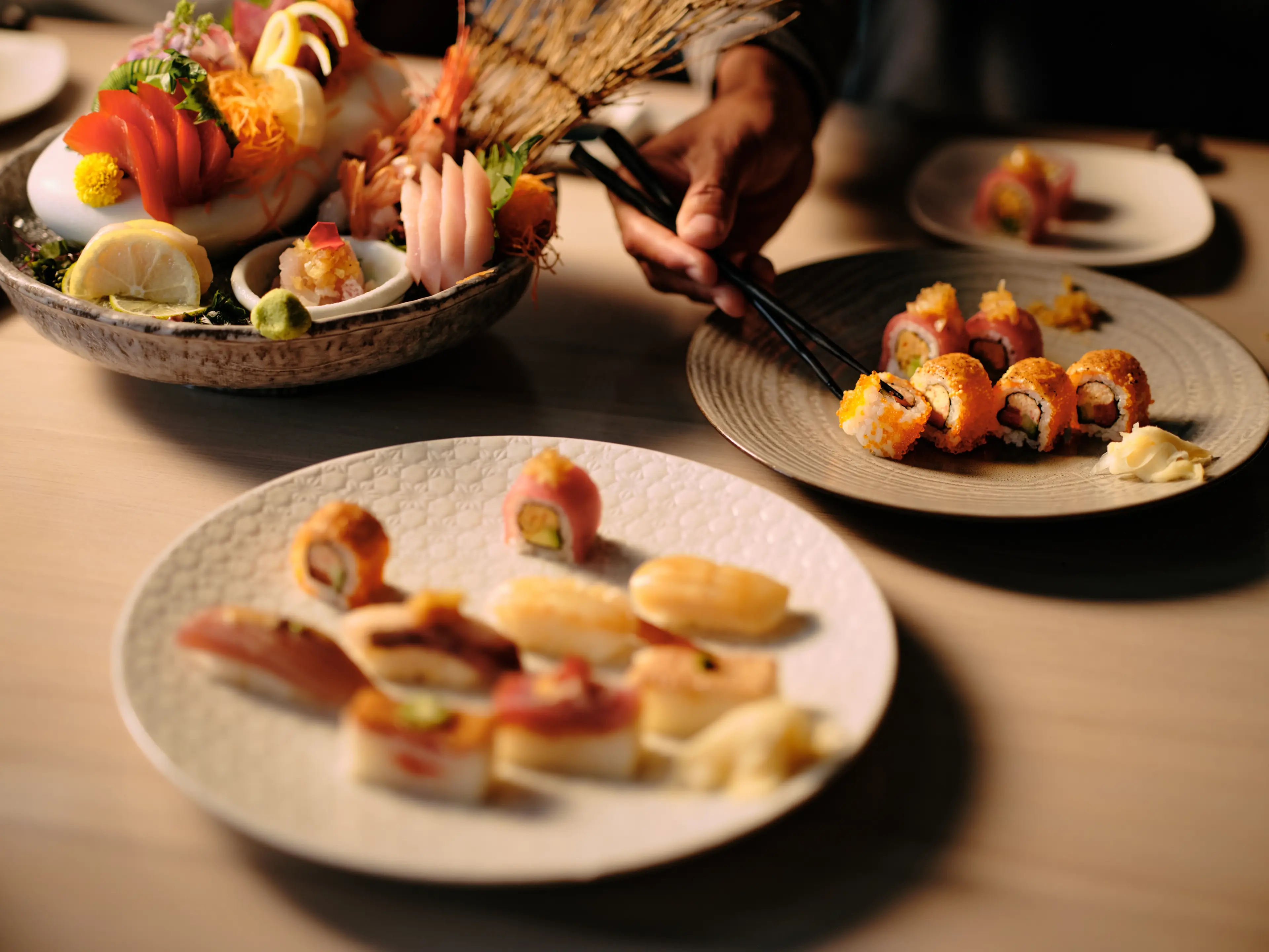 A photo of sushi plates thoughtfully decorated and a hand reaching in with chop sticks to grab a sushi at the Miku restaurant in Vancouver.